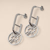 Pair of silver hoop earrings with geometric designs on a beige background